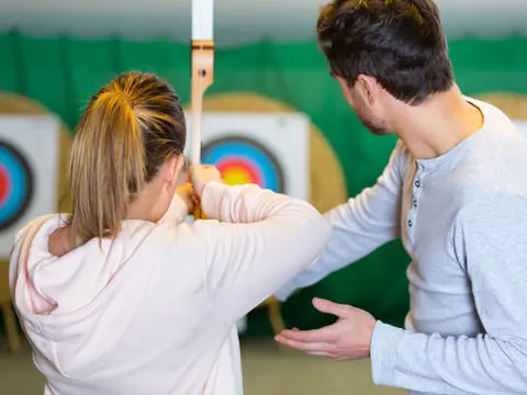 Trainer korrigiert eine Frau beim umgang mit dem Bogen